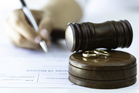 Woman signing divorce papers near a judge's gavel with wedding rings on the block