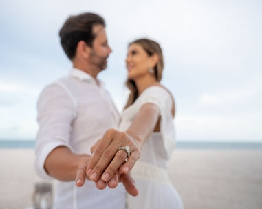 couple on the beach holding out their hands showing off engagement ring