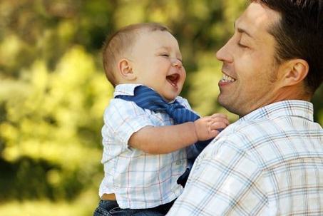 A father holding his baby. Both are smiling.