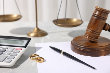 Alimony. Wedding rings, calculator, document, pen, scales and gavel on grey marble table, closeup
