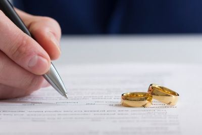 a person signs divorce papers with two gold wedding rings sitting on top